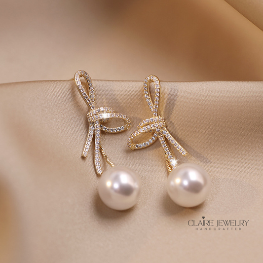 Pearl earrings with a glossy bow in gold